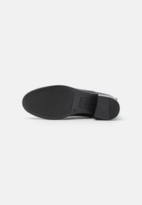 Semelle de chaussure noire avec un motif texturé, présentant un design solide et un talon légèrement surélevé pour un soutien et une adhérence supplémentaires.