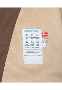 Étiquette d'une veste imperméable et respirante avec des instructions d'entretien sur un fond en tissu crème, comportant un accent marron et plusieurs icônes.