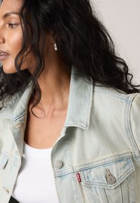 Ανοιχτό μπλε τζιν μπουφάν με μεταλλικά κουμπιά, δύο τσέπες στο στήθος και απαλή υφή. Διαθέτει κανονικό γιακά και εμφανείς λεπτομέρειες ραφής.