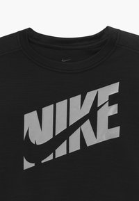Svart sporttröja i tyg med en stor, framträdande grå Nike-logotyp över framsidan. Den har rund halsringning och en mjuk textur.