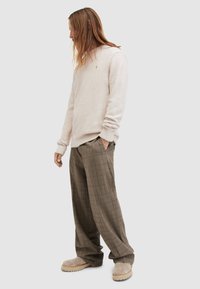 Helles beiges Sweatshirt mit gerippten Bündchen, kombiniert mit braunen Hosen im Kariertdesign. Füße in hellbeigen Schuhen.