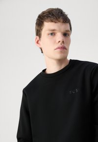 Crna dukserica s okruglim izrezom i teksturiranim materijalom. Suptilni logo "BOSS" u boji koja se slaže na prsima.