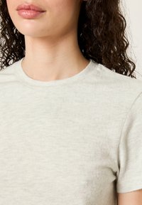 Gai pelēks īsām piedurknēm T-kreklis ar apaļu kakla izcirtni, izgatavots no mīksta, teksturēta auduma. Vienkāršs dizains, bez redzamām rakstām vai akcentiem.