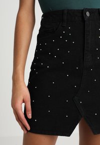 Černá džínsová sukně s A-liniovým střihem, předním rozparkem a rozptýlenými duhovými hroty pro dekorativní detaily.