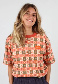 T-shirt à manches courtes, à motifs, en orange, rouge et vert avec des motifs floraux, doté d'un col rond et du logo OX BOW sur la poitrine.