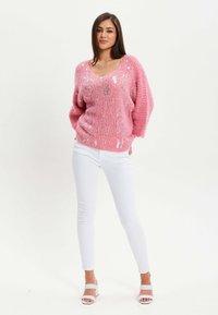 Pink knit sweater with a V-neck, featuring shiny silver accents. Paired with white skinny jeans and light-colored sandals.