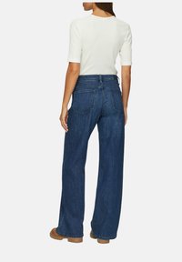 Široke jeans hlače iz denima v temno modri barvi z visokim pasom, dvema zadnjima žepoma in gladko teksturo. V kombinaciji z oprijetim belim zgornjim delom.