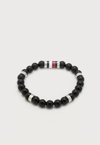 Μαύρο βραχιόλι με χάντρες και ασημένιες διαχωριστικές χάντρες, με μία ασημένια χάντρα που φέρει κάθετες κόκκινες, λευκές και μπλε ρίγες, σε λευκό φόντο.