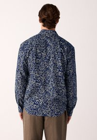 Siniste ja valgete lillemustriga pikkade varrukatega särk, millel on nööpidega krae ja lõdvestunud lõige. Materjal tundub õhuke ja tekstuuriga.