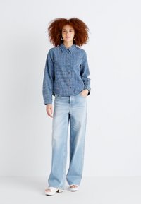 Blue checkered button-up shirt with long sleeves, paired with light blue wide-leg jeans and white platform sandals.