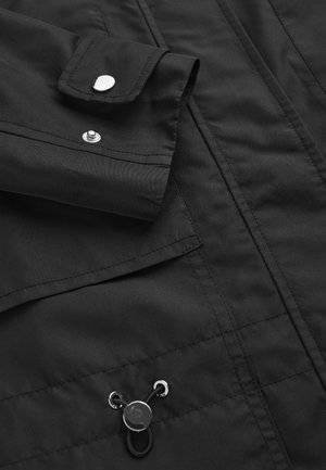 Zwarte stoffen jas met een zilveren drukknoop en verstelbare trekkoord met metalen oogjes.