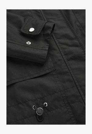 Zwarte stoffen jas met een zilveren drukknoop en verstelbare trekkoord met metalen oogjes.