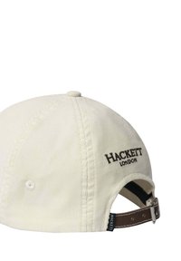 Cream-colored corduroy cap with adjustable brown leather strap and black "Hackett London" embroidery on the back.