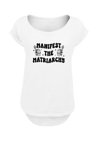 White t-shirt with a scoop neck and short sleeves. Features bold black text reading "Manifest the Matriarchy" with decorative elements.