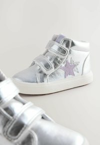 Baskets montantes métalliques argentées avec deux bandes Velcro, présentant un accent étoile violet sur le côté et des semelles blanches texturées.