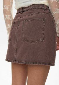 Brauner Denim-Minirock mit tailliertem Bund, sichtbaren Nähten, zwei Gesäßtaschen und einer Saumlinie, die kurz über dem Oberschenkel endet.