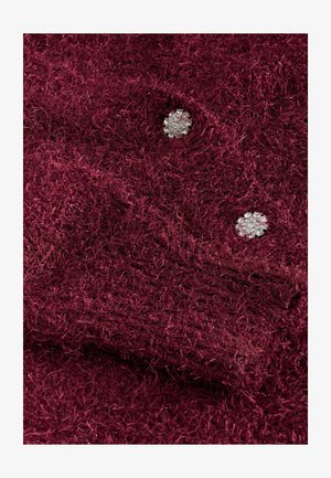 Tissu texturé bordeaux avec des fibres douces et deux appliqués décoratifs en forme de fleurs, ressemblant à des cristaux.