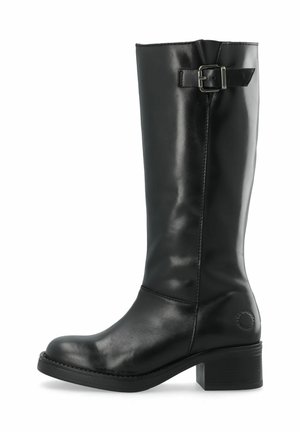 Botte haute en cuir noir avec un talon bas et carré et une sangle décorative avec boucle près du sommet sur fond blanc.