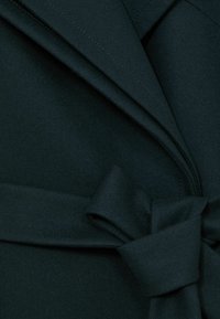 Tume roheline villane mantel laia kraega ja kangast vöö, mis on vööl lahti seotud.