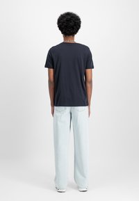 Mørkeblå t-shirt med korte ærmer, rund halsudskæring, parret med lyseblå brede jeans og hvide sneakers. Glat stof, afslappet pasform.