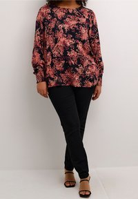 Blusa de manga larga floral en azul marino con patrones en rosa y coral, combinada con pantalones ajustados negros y sandalias negras con tiras.