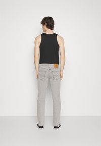 Grå jeans med en lærrem på baksiden av livet, parret med en svart tanktopp. Har rette ben og et klassisk fem-lomme-design.