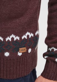 Pullover lavorato a maglia bordeaux con motivi geometrici bianchi e blu sull'orlo, presenta un'etichetta in pelle marrone con il nome del marchio !SOLID.