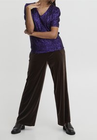 Lila paljetterad v-ringad topp med korta puffärmar, kombinerad med lösa, bruna sammetsbyxor och svarta loafers. Enkelt men med textur.