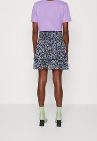 Černá květinová mini sukně s vrstvenými volány a vzorem v modré, zelené a bílé barvě; doplněná levandulovým tričkem s krátkým rukávem a zelenými lodičkami.