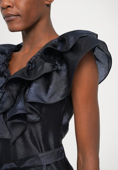 Mørk navy kjole med struktureret stof, voluminøse skuldre og en indsnævret talje. Materialet har en glansfuld glød og en subtil fald.