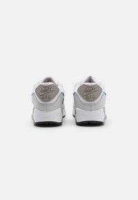 Sapatilhas Nike Air com uma parte superior em malha branca e couro cinza, apresentando um destaque azul e o logo no calcanhar, sola de borracha texturizada.