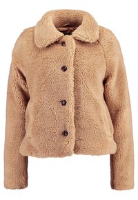 Tan faux fur-jacka med krage, fem bruna knappar och strukturerad tyg, med en boxig form och långa ärmar.
