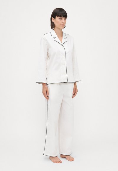 Set de pijama alb, cu mâneci lungi, detalii cu piping negru, închidere cu nasturi și pantaloni drepți. Material neted, design minimalist.