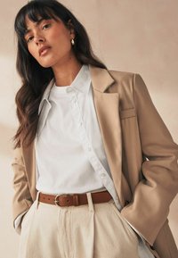 Beige blazer over white shirt, brown leather belt, cream pants, with smooth fabric textures and minimalistic design details.
