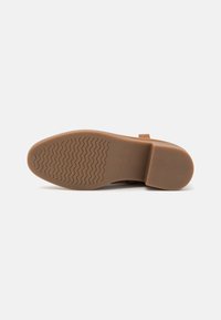 Suela de goma marrón con un patrón de banda de rodadura ondulado, que presenta una puntera redondeada y un detalle de correa lateral. Textura suave con un tacón plano.