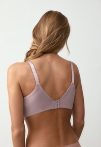 Soutien-gorge mauve clair avec bretelles réglables, texture lisse et dos en forme de V. Comprend trois crochets pour la fermeture.