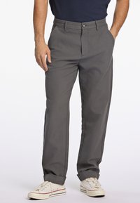 Pantalons gris à jambe droite avec une texture lisse, fermeture à bouton et deux poches latérales, associés à des baskets écrues avec des accents rouges.