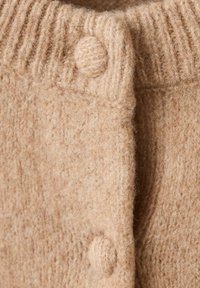 Cárdigan de lana beige con un collar acanalado, que presenta un acabado texturizado y botones redondos. La tela parece suave y ligeramente peluda.