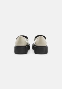Patente zwarte platformklompen met een gladde beige bovenkant en open achterkant. Getextureerde rubberen zool met uitgesproken ribbels voor grip.