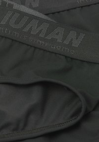Schwarze Herrenunterwäsche mit einem strukturierten Taillenbund, auf dem "HUMAN" steht, und aus einem weichen, glatten Stoff mit nahtlosem Design.