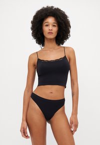 Set di lingerie nera composto da un canotto aderente con bordo in pizzo e mutandine a vita alta coordinate, realizzato in materiale liscio ed elastico.