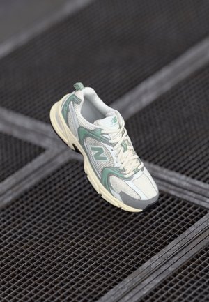 Chaussure de course blanche et vert menthe avec lacets reposant sur une surface en grille métallique, inclinée pour montrer la vue latérale et la vue de dessus.