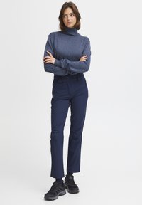 Pull à col roulé bleu marine avec manches longues, associé à un pantalon noir marine ajusté et des chaussures de sport noires. Texture de tissu lisse.