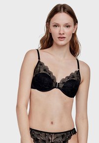 Soutien-gorge en dentelle noire avec des bonnets rembourrés, broderie florale le long des bords, bretelles réglables et fermeture à crochets au centre avant.