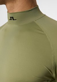 Olivgrön åtsittande atletisk topp med hög krage, svart logodetalj vid nacken och slät syntetisk tyg för ett elegant utseende.