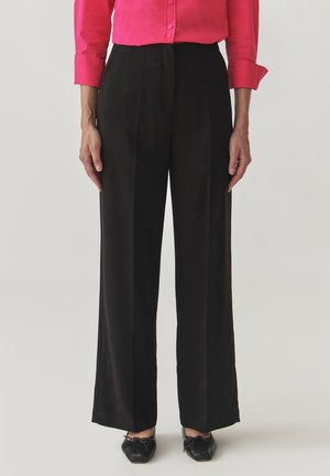 Black wide-leg trousers with a tailored fit, featuring a smooth texture and pleated front. Paired with a bright pink, button-up blouse.