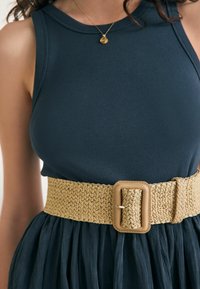 Dunkelblaues geripptes Tanktop, kombiniert mit einem breiten gewebten Strohgürtel mit einer beigefarbenen Kunstleder-Schnalle und einer strukturierten Oberfläche.