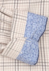 Wollen blend stof met een lichtbeige ruitpatroon en grijze accenten; heeft een blauwe geometrisch patroon manchette met donker accent.