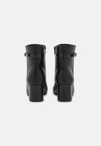 Botas de cuero negro hasta el tobillo con un acabado liso, tacones gruesos y correas ajustables en el tobillo. Diseño minimalista sin patrones visibles.