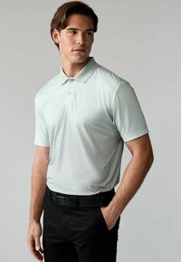 Hellgrünes Poloshirt mit strukturiertem Muster, kurzen Ärmeln und Kragen, kombiniert mit schwarzen Hosen und einem schwarzen Gürtel.